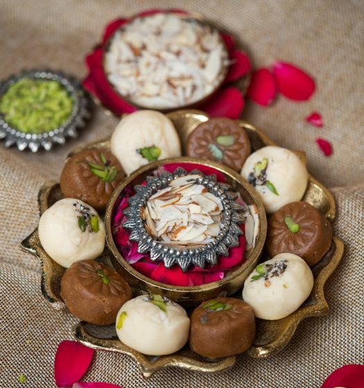 Assorted Indian sweets beautifully arranged on a decorative platter with rose petals, creating a festive feel.